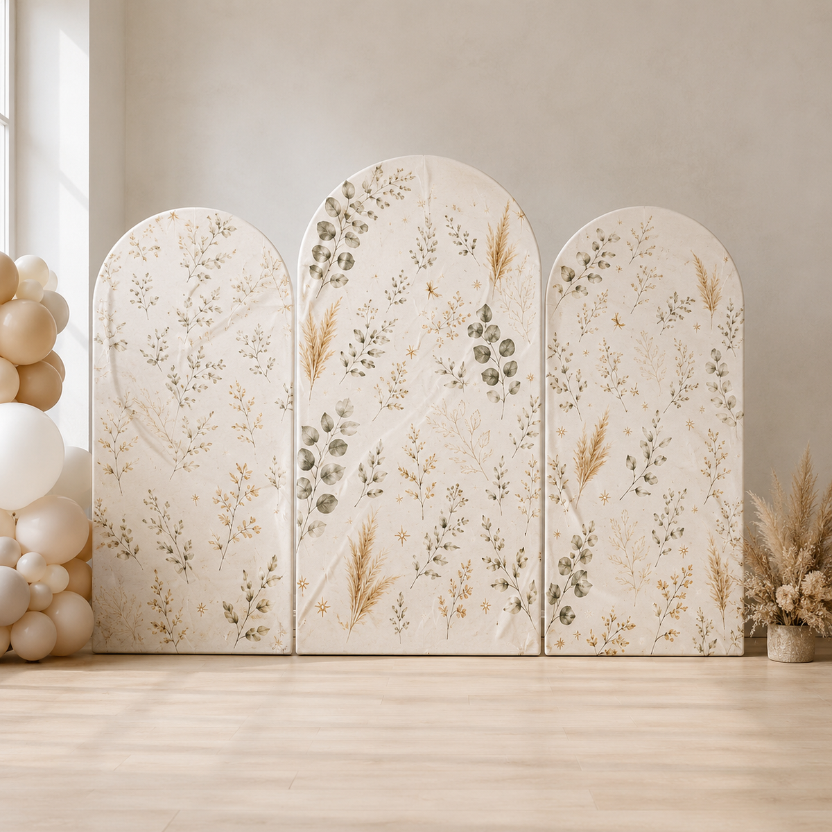 Three arched fabric panels with a beige botanical pattern, arranged as a temporary backdrop in a neutral studio setting with decorative balloons and dried grass on the sides.