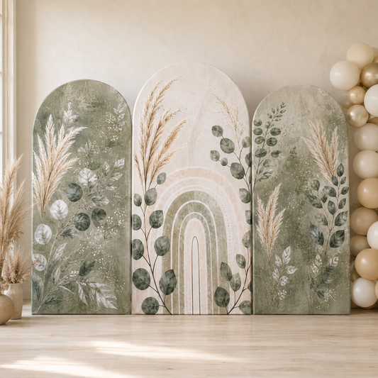 Three arched decorative party backdrops with a boho botanical and rainbow design, displayed on a light wood floor against a beige wall with balloon garlands.